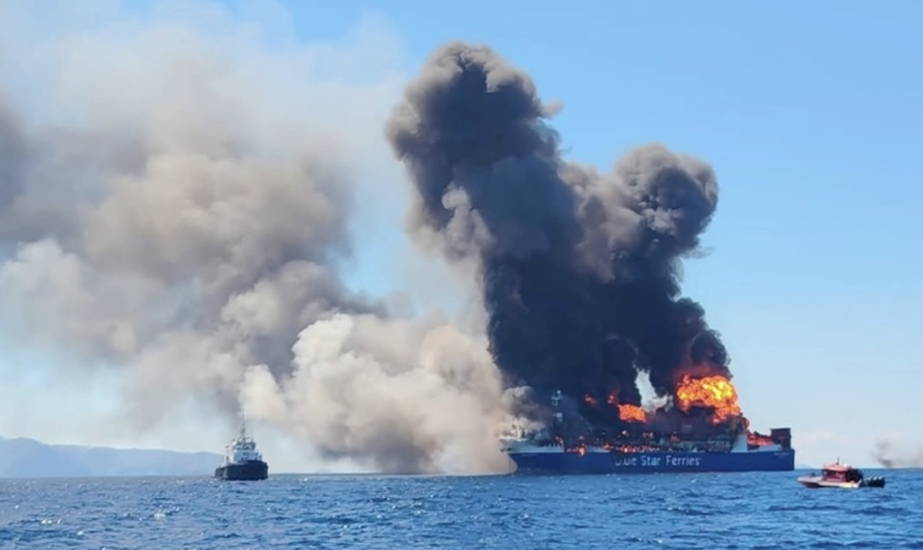 Vehicle-transporting vessel towed clear of Mykonos as fire still burns