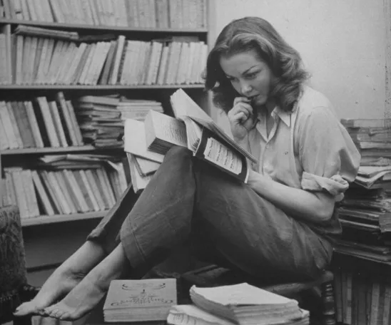 Sylvia Plath in familiar guise, surrounded by books.